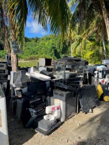 Large pile of discarded electronic waste including TVs, printers and computers under palm trees in the Pacific.